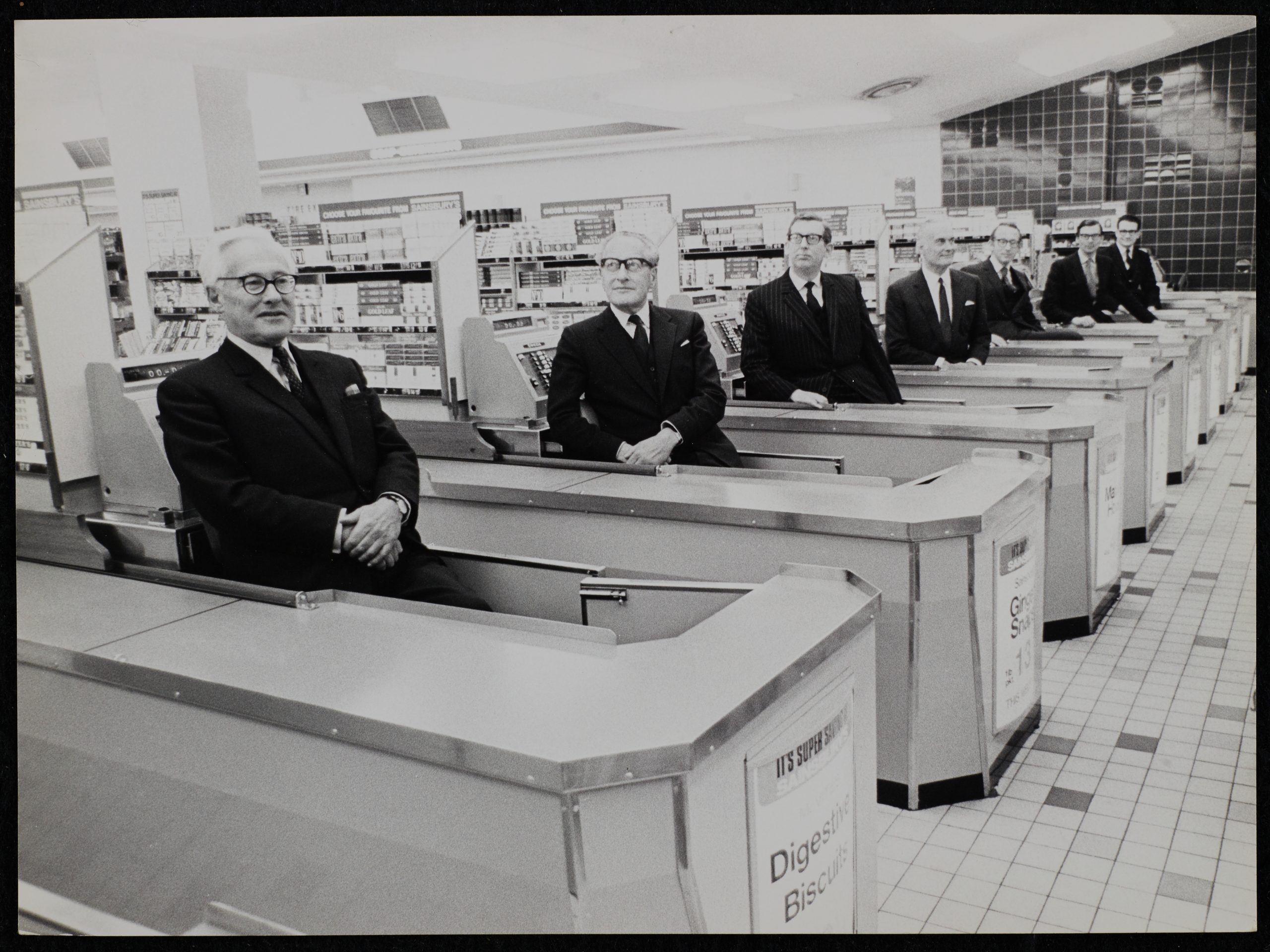 Seven Sainsbury family members sitting at tills in a Sainsbury's branch for a photoshoot.